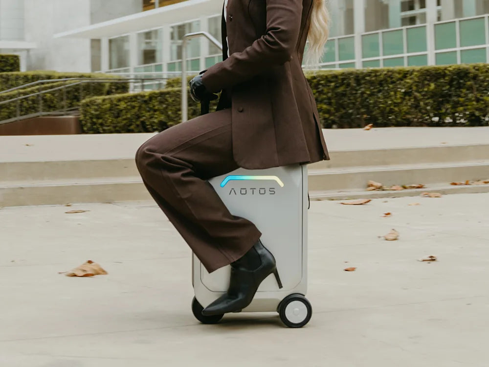 Business professional riding an AOTOS smart rideable suitcase across an urban plaza, highlighting its electric, hands-free carry-on mobility.