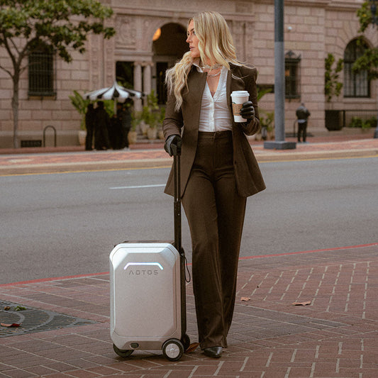 Professional businesswoman pulling an AOTOS L2 rideable smart electric suitcase on a city street while holding a takeaway coffee.
