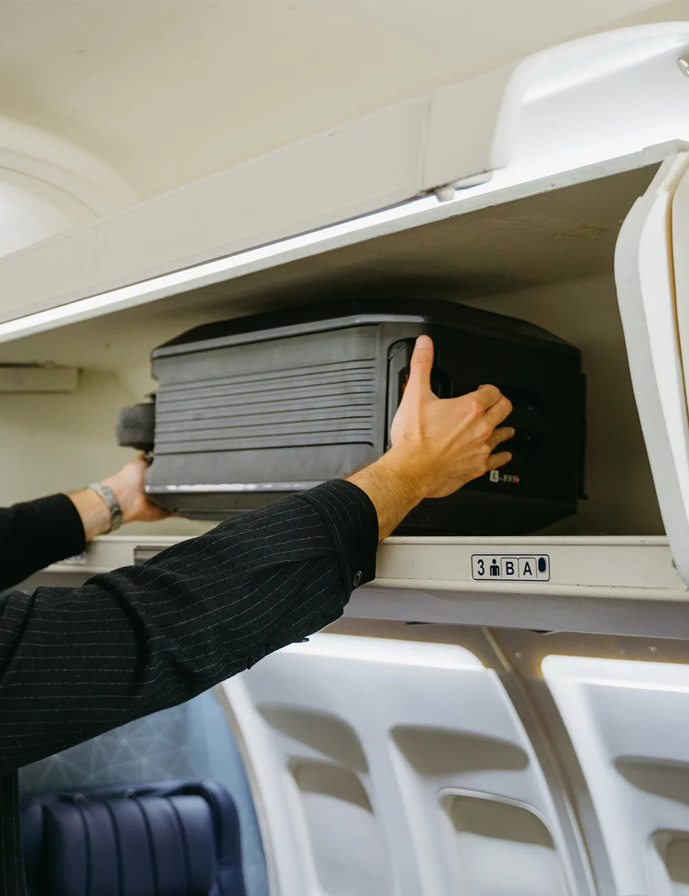 Traveler sliding an AOTOS L2 smart rideable carry-on into an airplane overhead bin — compact, FAA-compliant electric luggage that fits standard cabin space