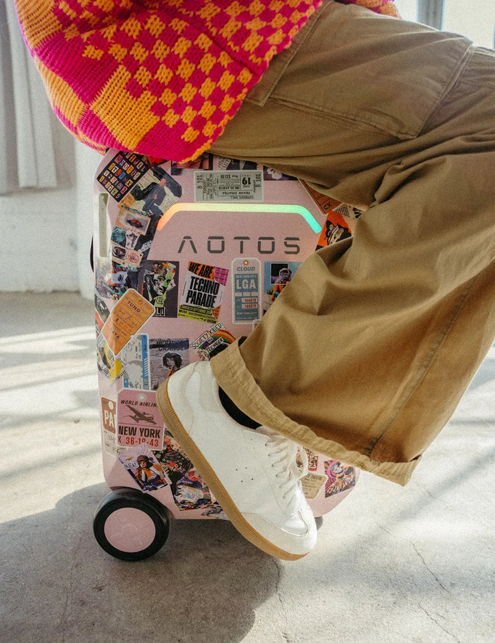 Sticker-covered pink AOTOS L2 rideable suitcase doubled as a seat — customizable electric carry-on with eye-catching LED logo