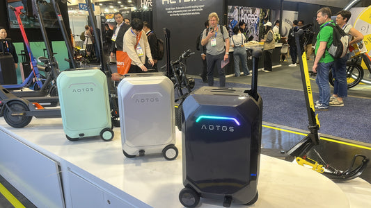 Three AOTOS smart rideable suitcases displayed at a travel gear exhibition, showcasing modern luggage technology with sleek hard-shell designs and built-in wheels.