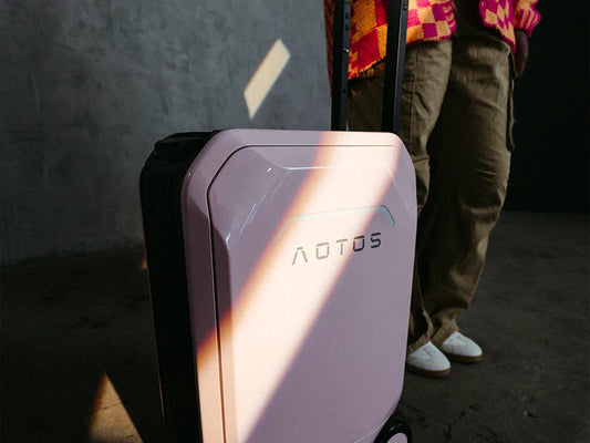 Close-up of pastel pink AOTOS smart rideable suitcase under a dramatic beam of sunlight, highlighting its sleek cabin-friendly design and telescopic handle.