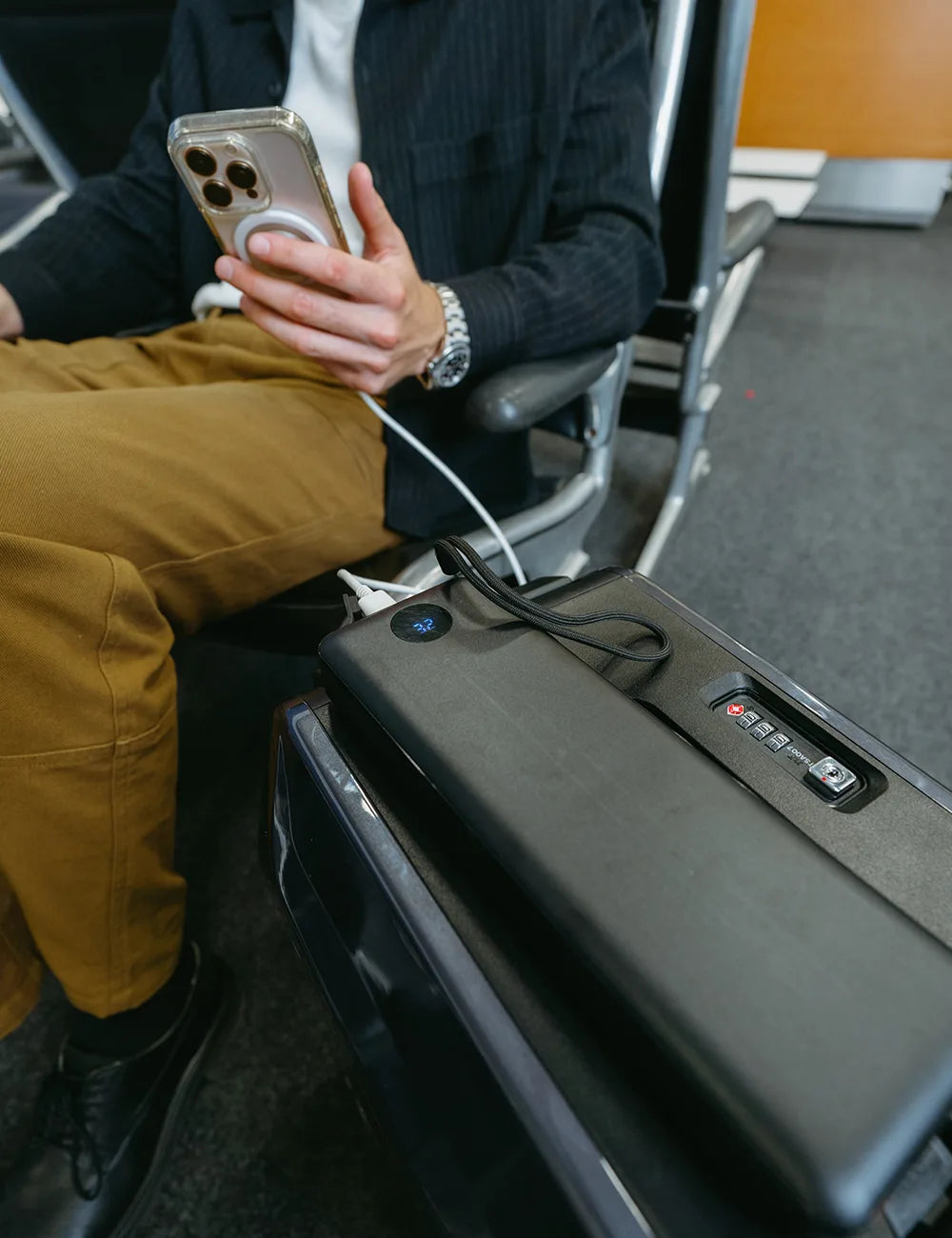 Removable AOTOS L2 lithium battery pack charging a smartphone via USB in an airport lounge, with TSA-approved combination lock in view